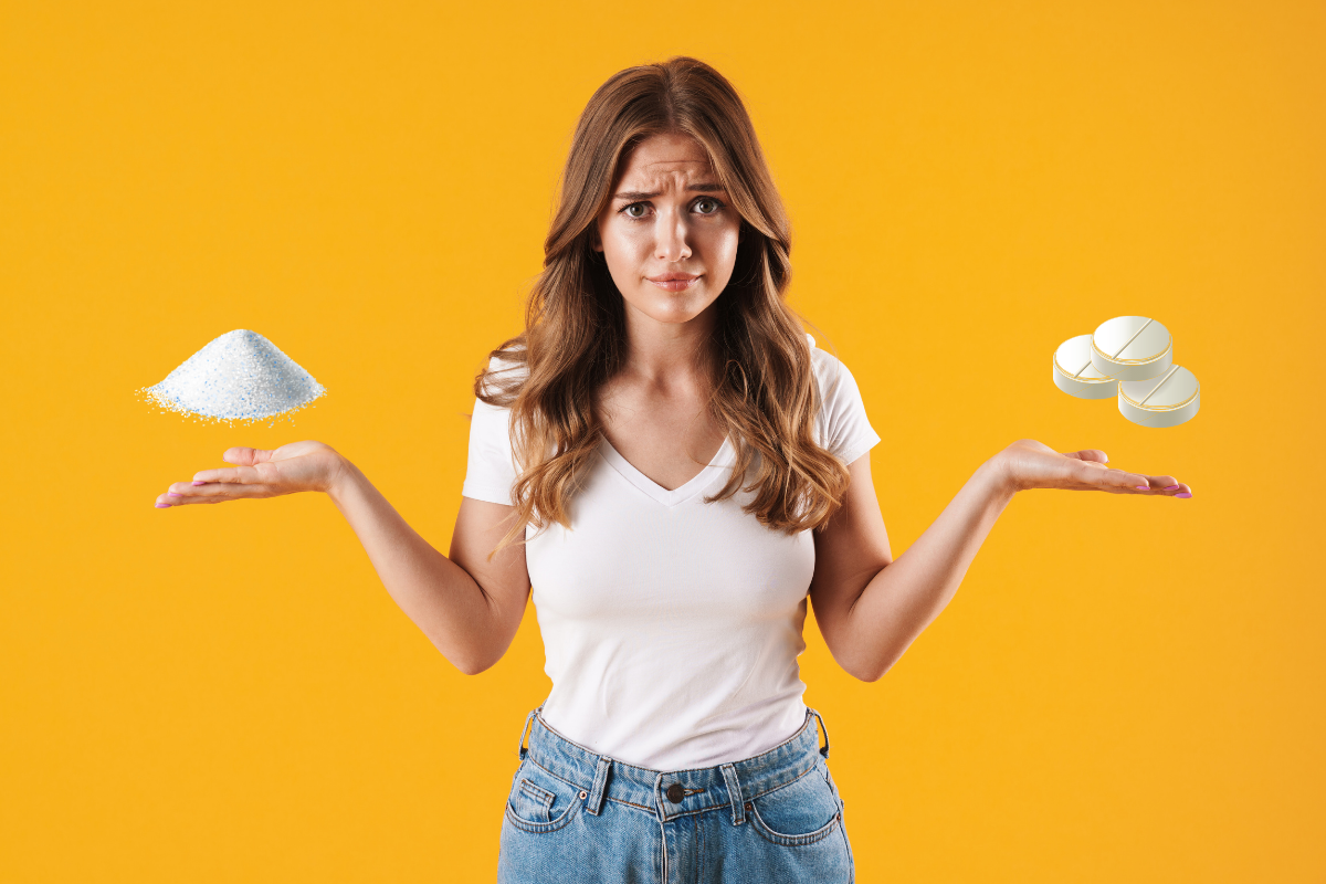 A woman in a white t-shirt and jeans stands against a bright orange background, looking puzzled as she holds a pile of powder in one hand and several capsules in the other.