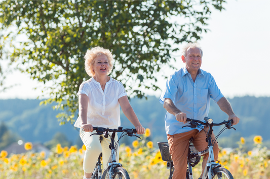 Happy elderly couple smiling while riding a bicycle together outdoors in a grassy field, enjoying leisure time and staying active.