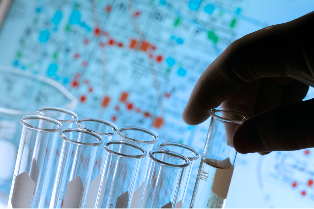 Hand reaching for laboratory test tubes against a blue background.