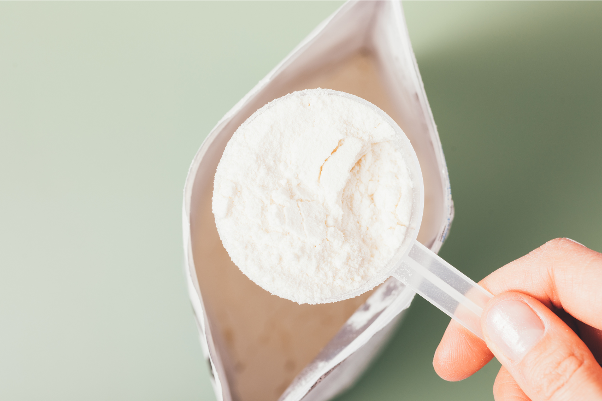 A hand holding a scoop of white powder over an open package.