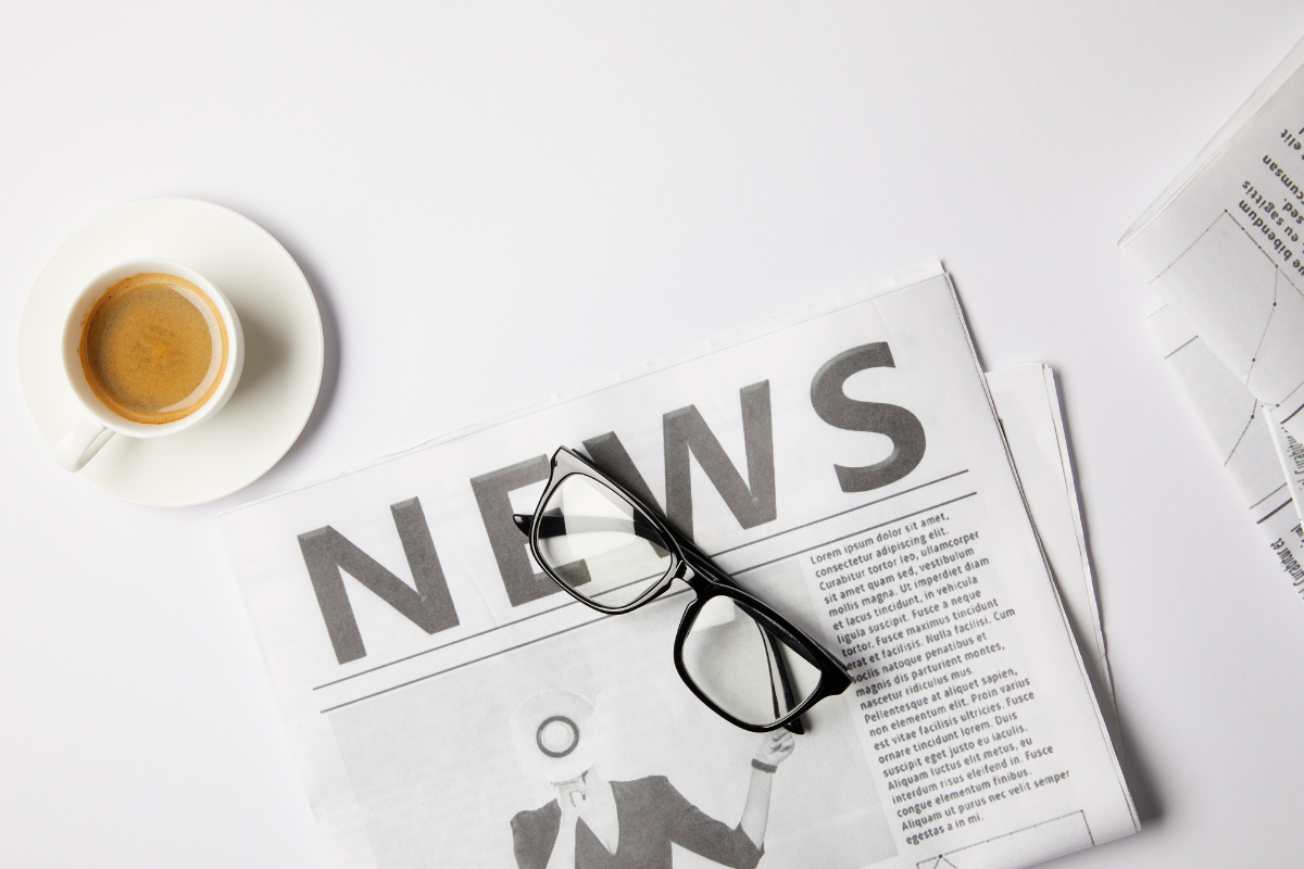 A cup of coffee, a pair of glasses, and a newspaper on a table.