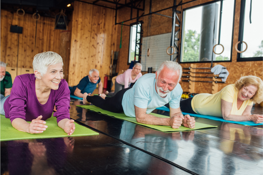 A group of smiling older people performing planks on mats.