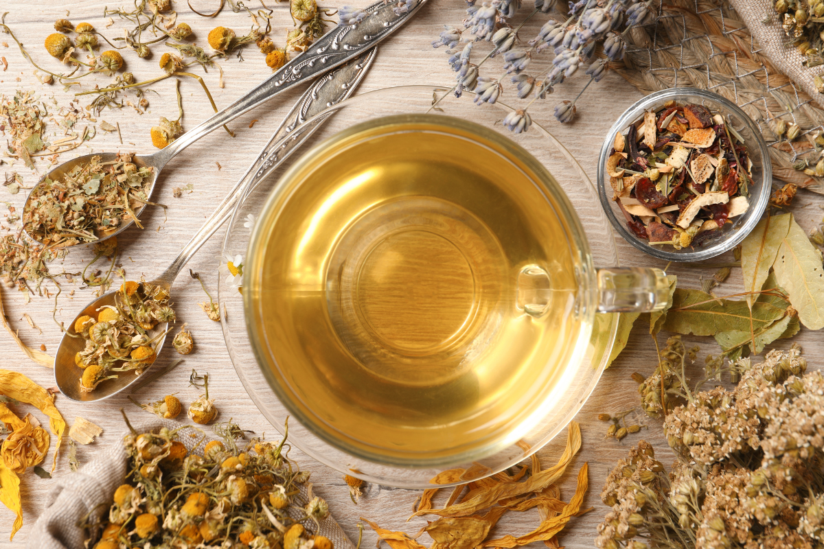 A cup of herbal tea surrounded by dried herbs and flowers.