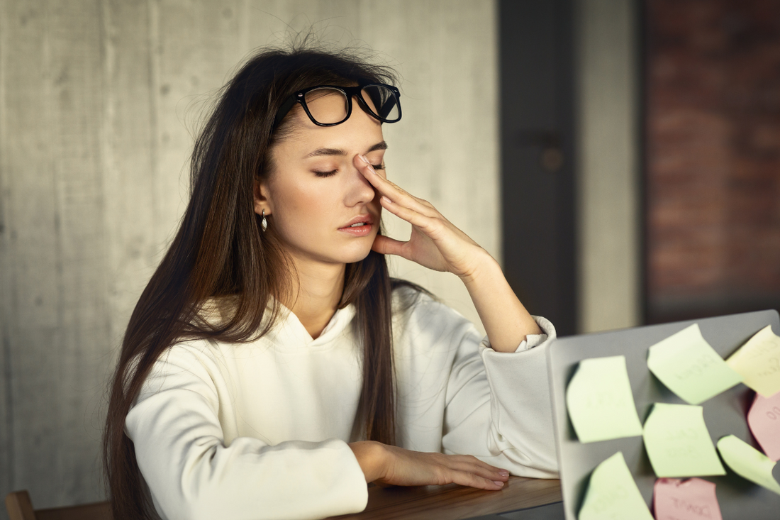 Tired young woman rubbing her eyes while sitting in front of a laptop.