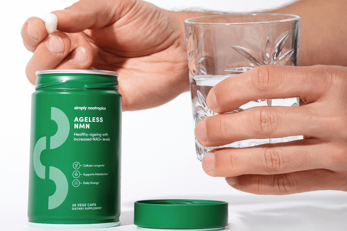 Person holding a Simply Nootropics Ageless NMN supplement capsule and a glass of water.