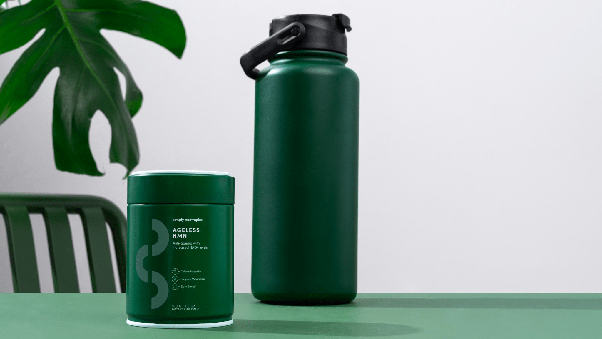 Ageless NMN supplement next to a green water bottle on a minimalist table with a leafy backdrop.