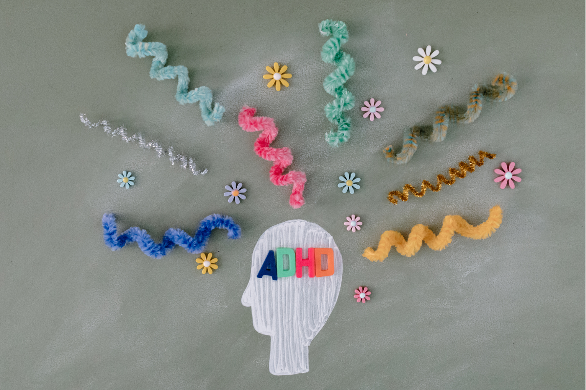 Colourful representation of ADHD with a silhouette head labelled "ADHD" and wavy lines and flowers symbolising cognitive activity and focus.