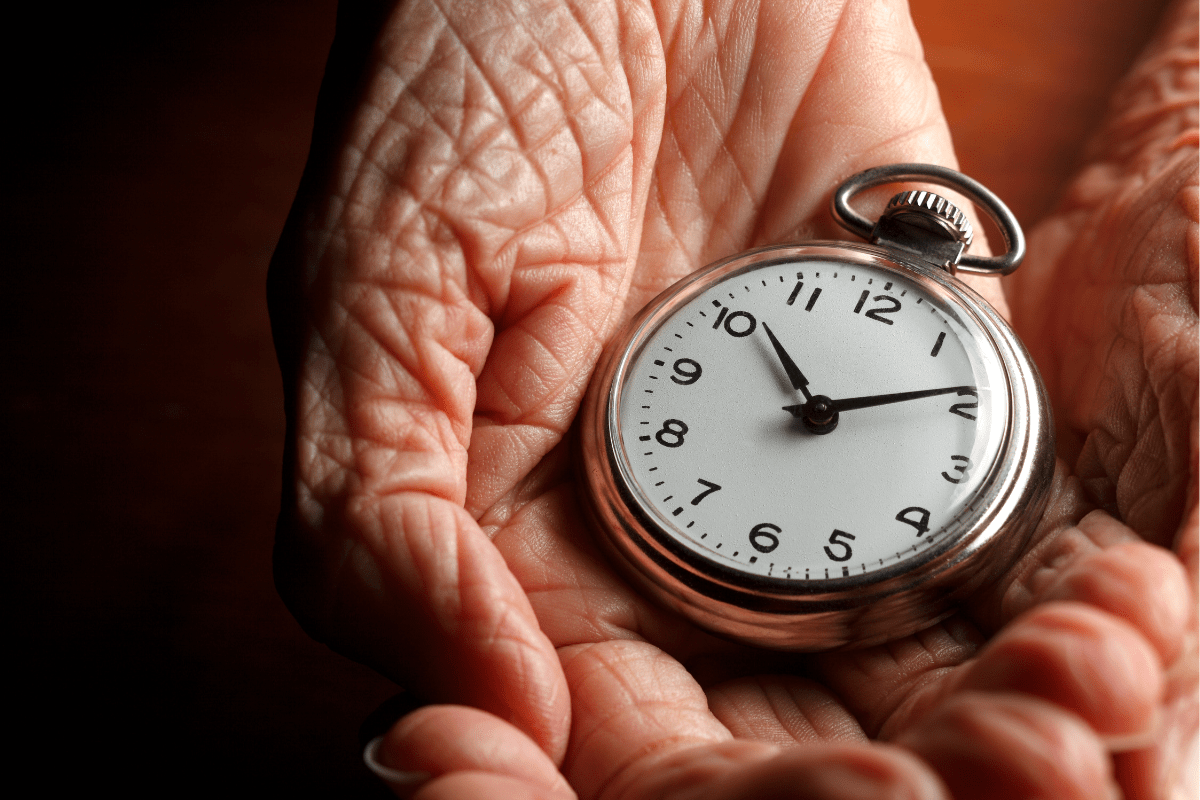 Wrinkled hands holding a pocket watch.