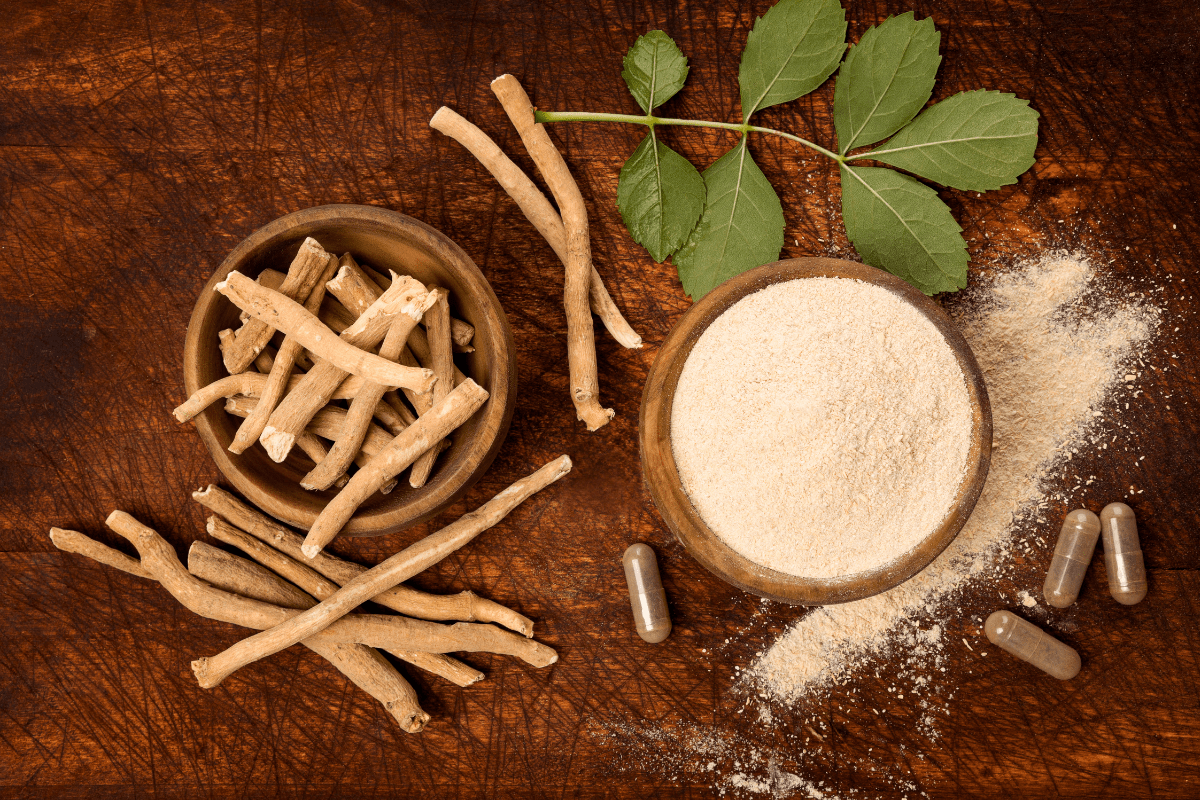 Ashwagandha roots, powder, and capsules displayed on a wooden table with fresh leaves.