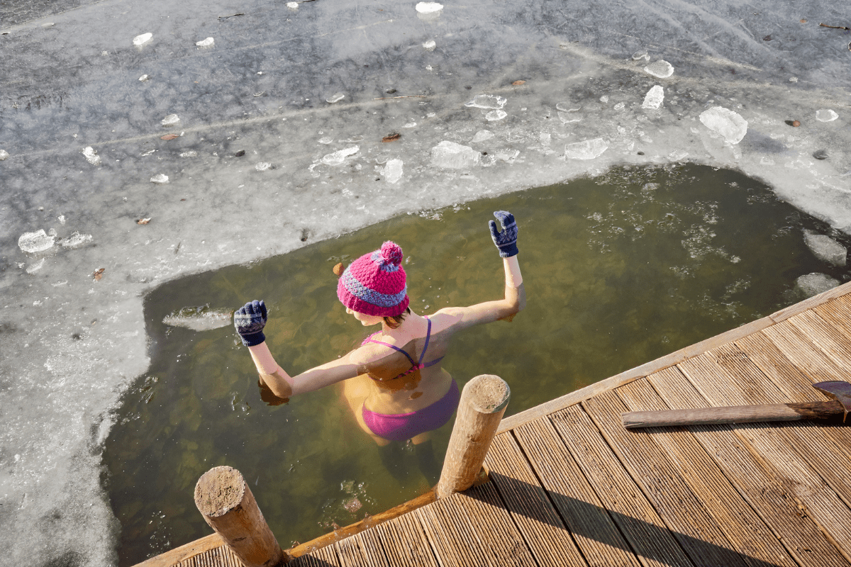 Woman in a bikini, gloves, and a winter hat immersing herself in an ice-cold lake.