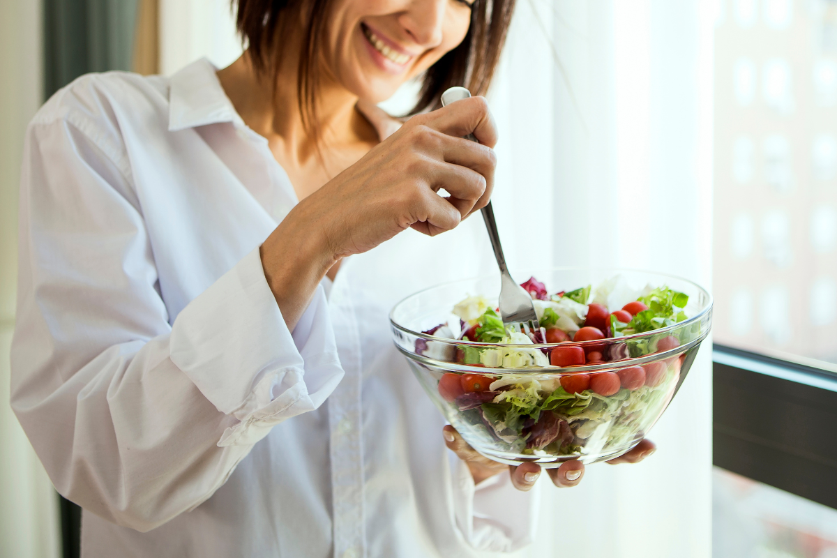 Woman holding a fresh salad bowl by a bright window.