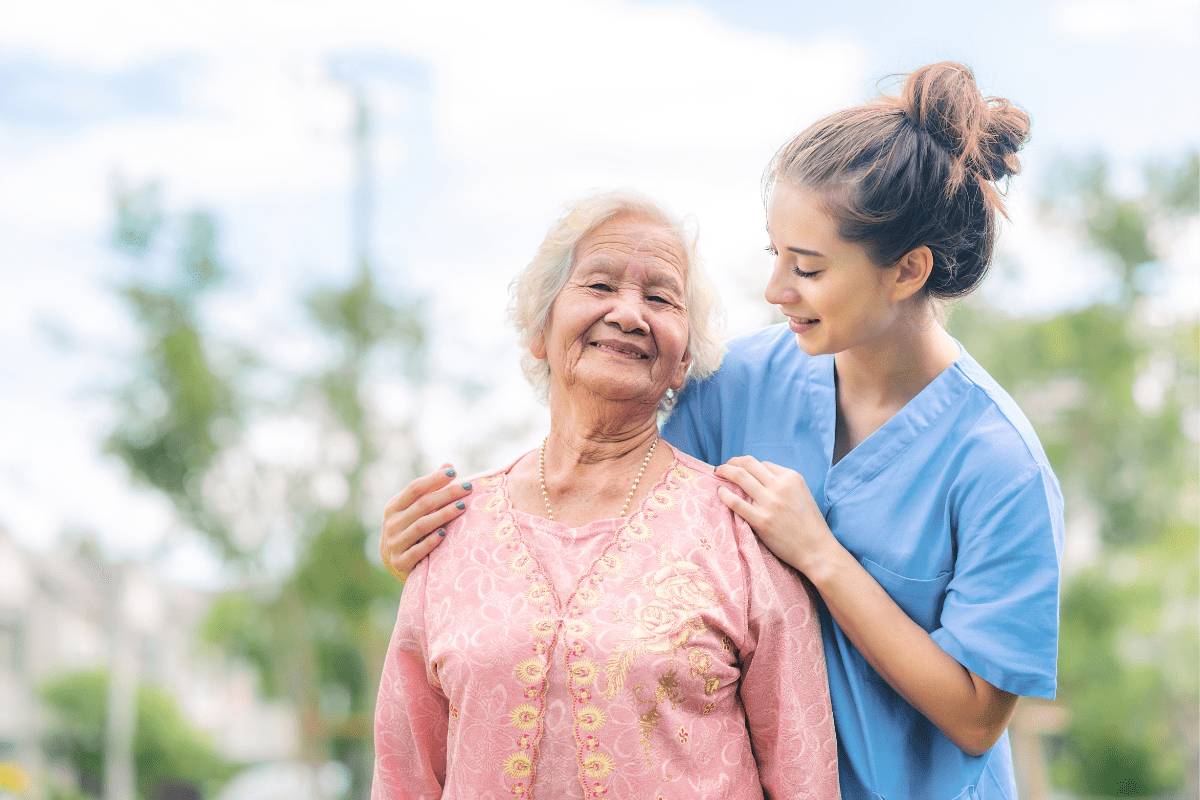 Smiling elderly woman outdoors with a younger caregiver.