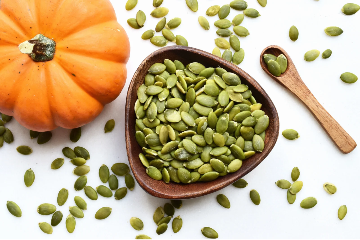 Pumpkin seeds in a wooden bowl beside a pumpkin.