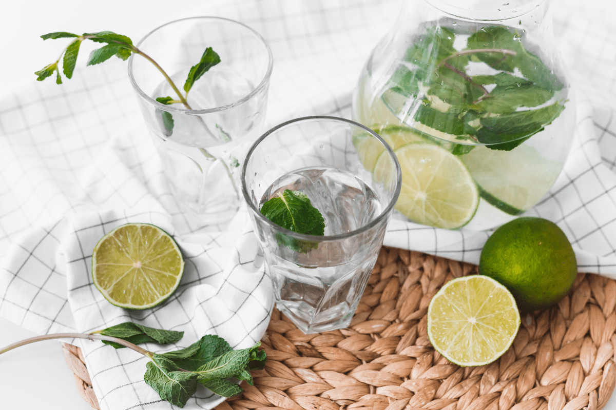 Glasses and a carafe of lime and mint water on a woven mat.