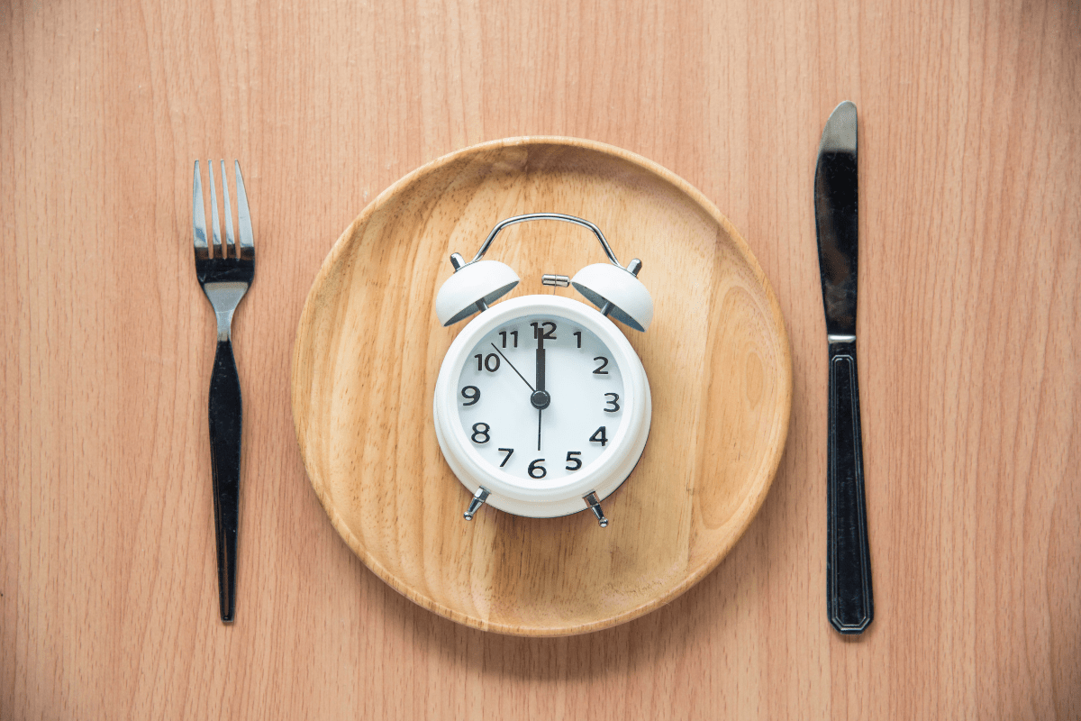 Plate with a clock in the center, surrounded by a fork and knife, symbolizing fasting and meal timing