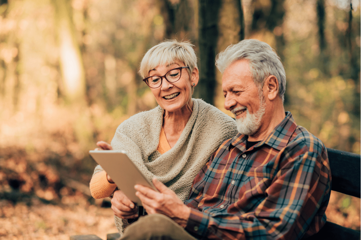 Older couple smiling while looking at a tablet together.