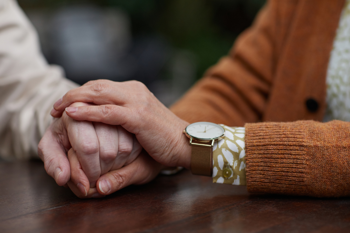 Close-up of two hands clasped together in a comforting gesture, showing support and care.