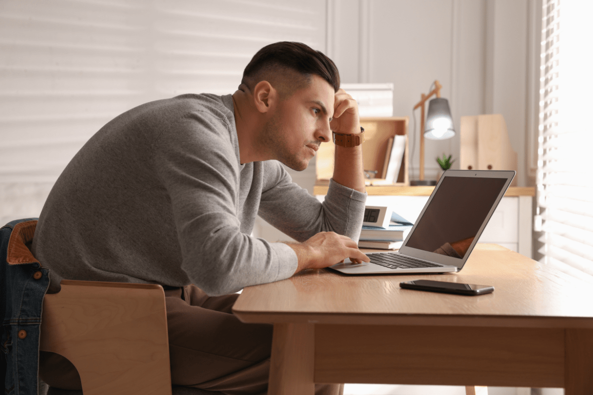 Man sitting at a desk, slouched over his laptop, with poor posture.