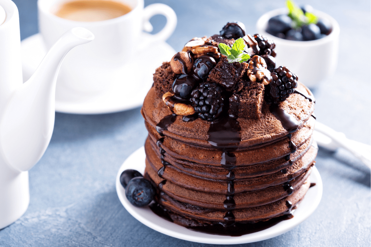 Stack of chocolate pancakes with sauce and toppings.