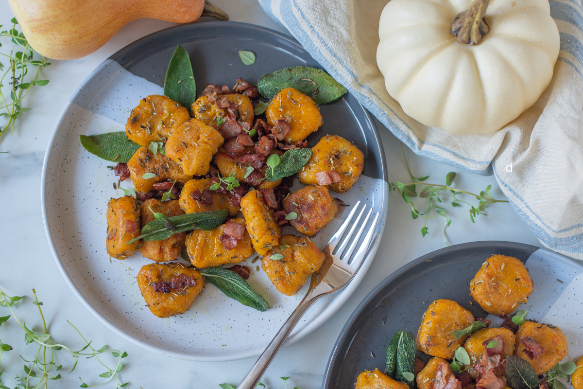 Pumpkin gnocchi with crispy sage, pecans, and herbs on a grey ceramic plate.