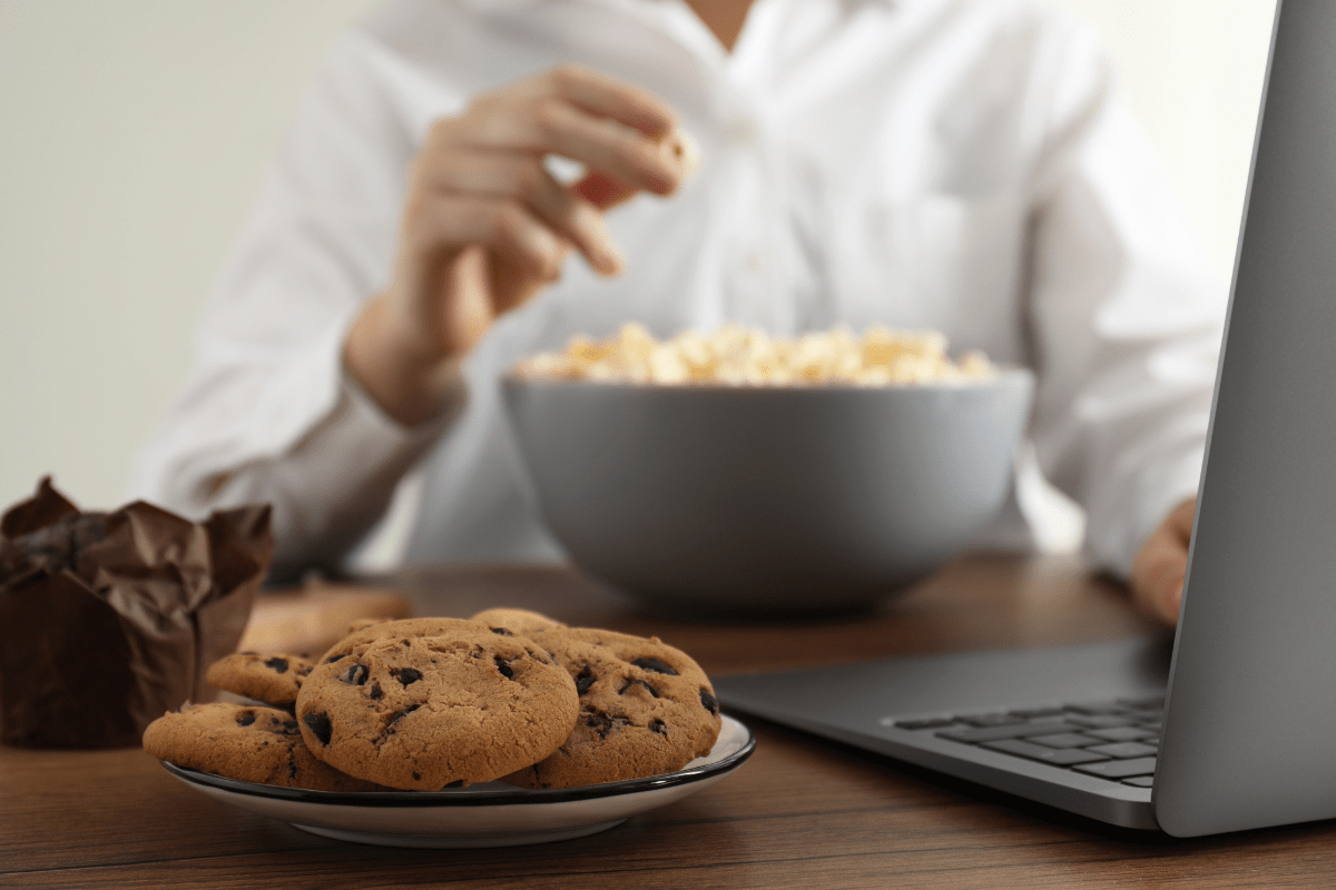 Person snacking at a desk with cookies, popcorn, and a laptop in view.