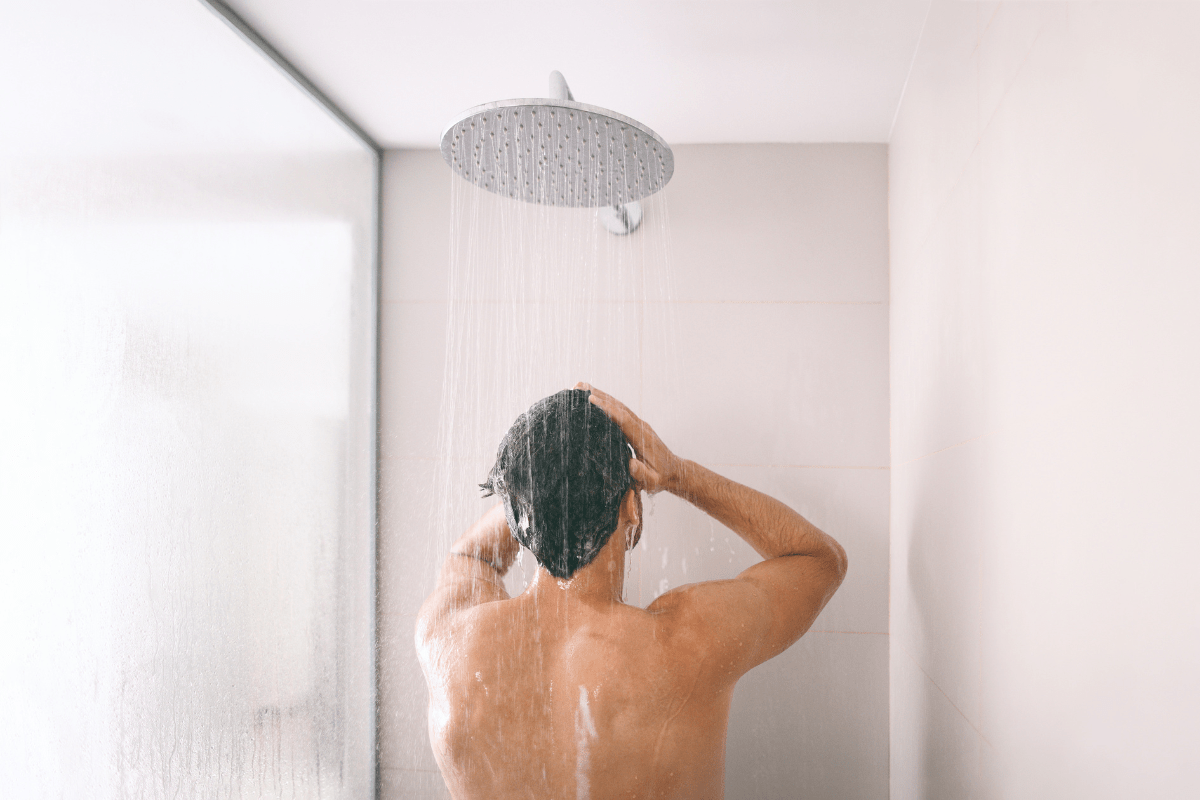 Man washing his hair under a running shower.