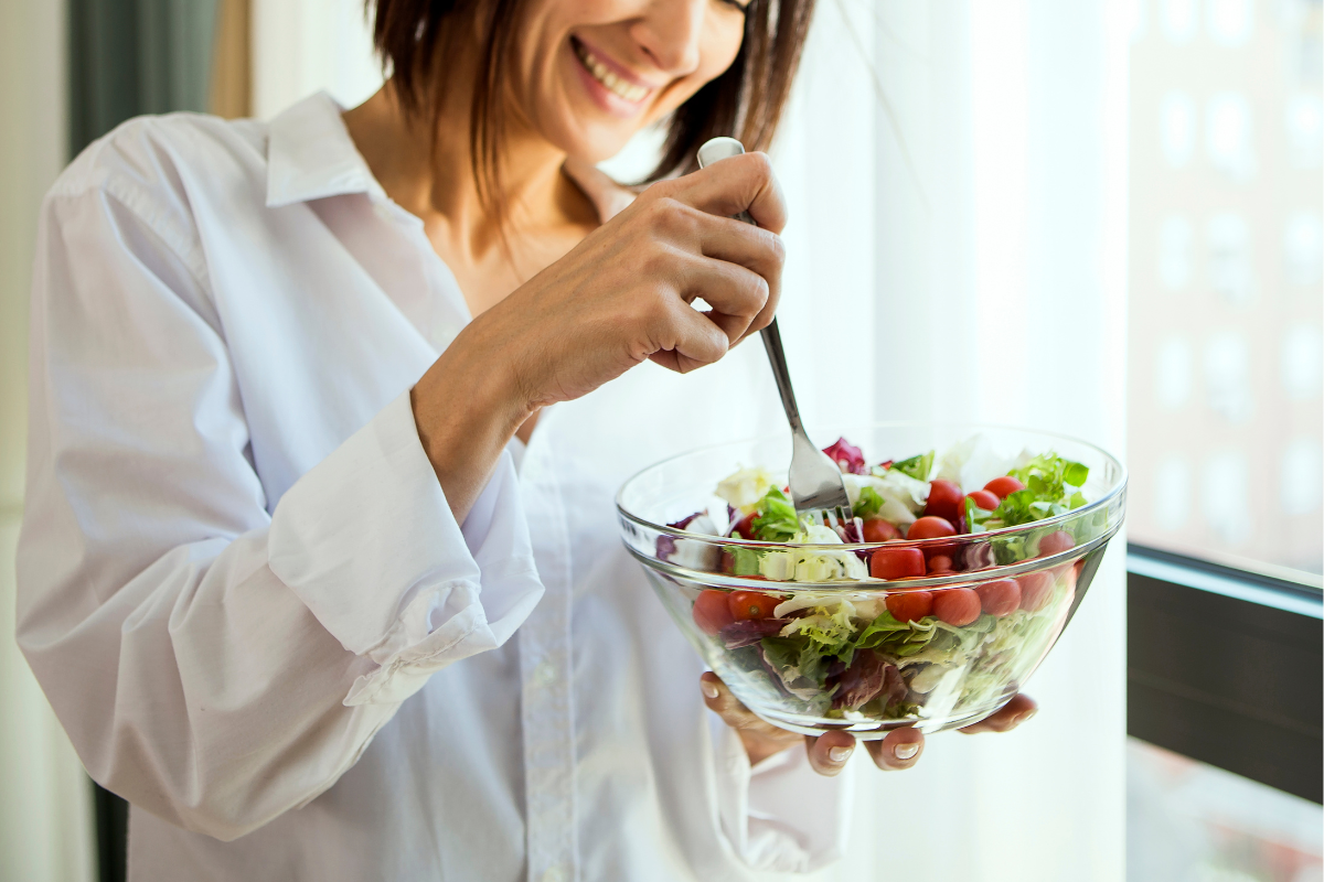 Woman smiling while eating a fresh salad from a glass bowl.