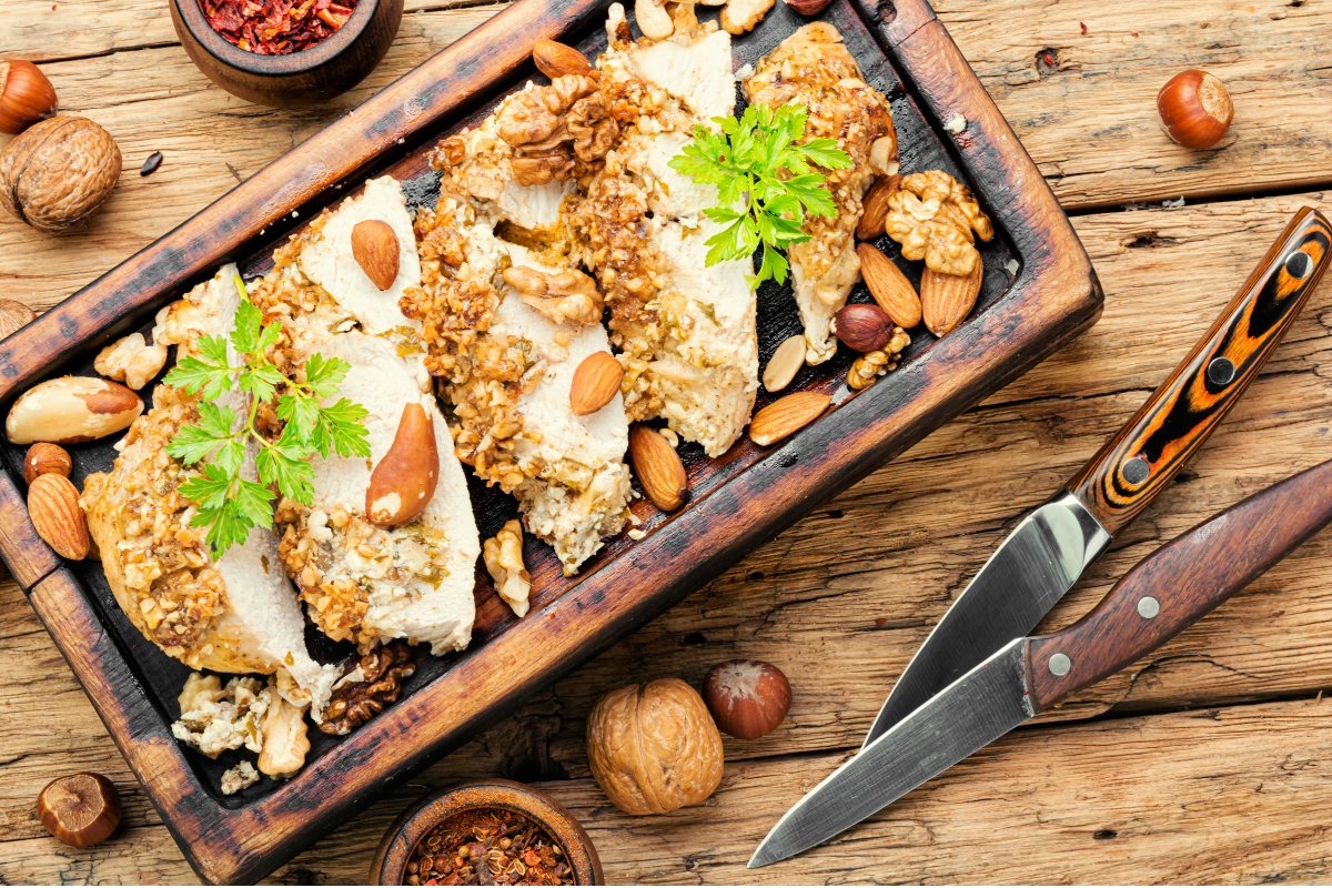 Almond-crusted chicken served on a wooden board with whole nuts and herbs.