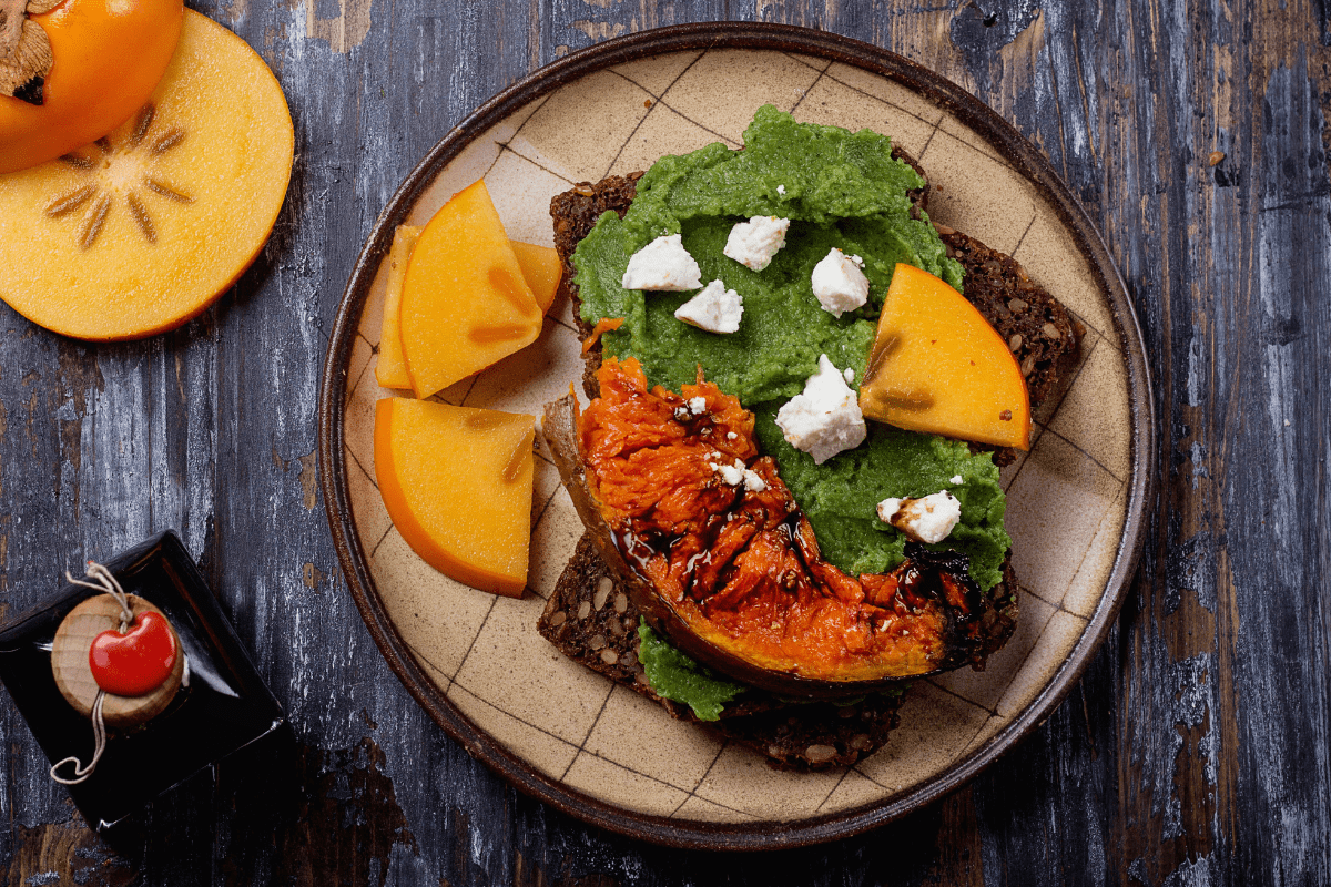 Sandwich topped with avocado, pumpkin, persimmon, and feta.
