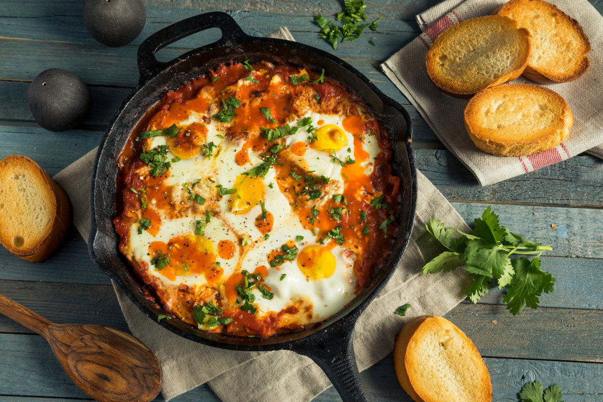 A skillet of freshly cooked Shakshuka, featuring poached eggs in a rich, spiced tomato and pepper sauce, garnished with chopped parsley.