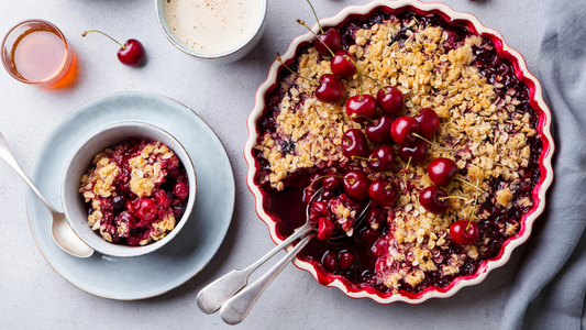 A cherry and red berry crumble in a baking dish placed on a grey stone background.